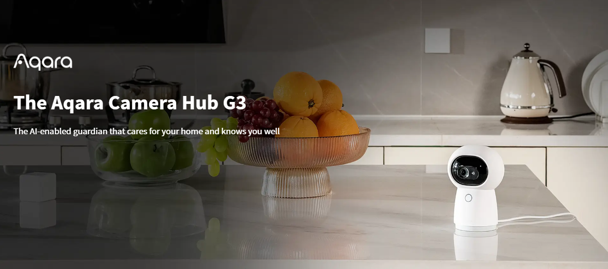 Aqara Camera Hub G3 on a kitchen counter with fruits and kitchen appliances in the background