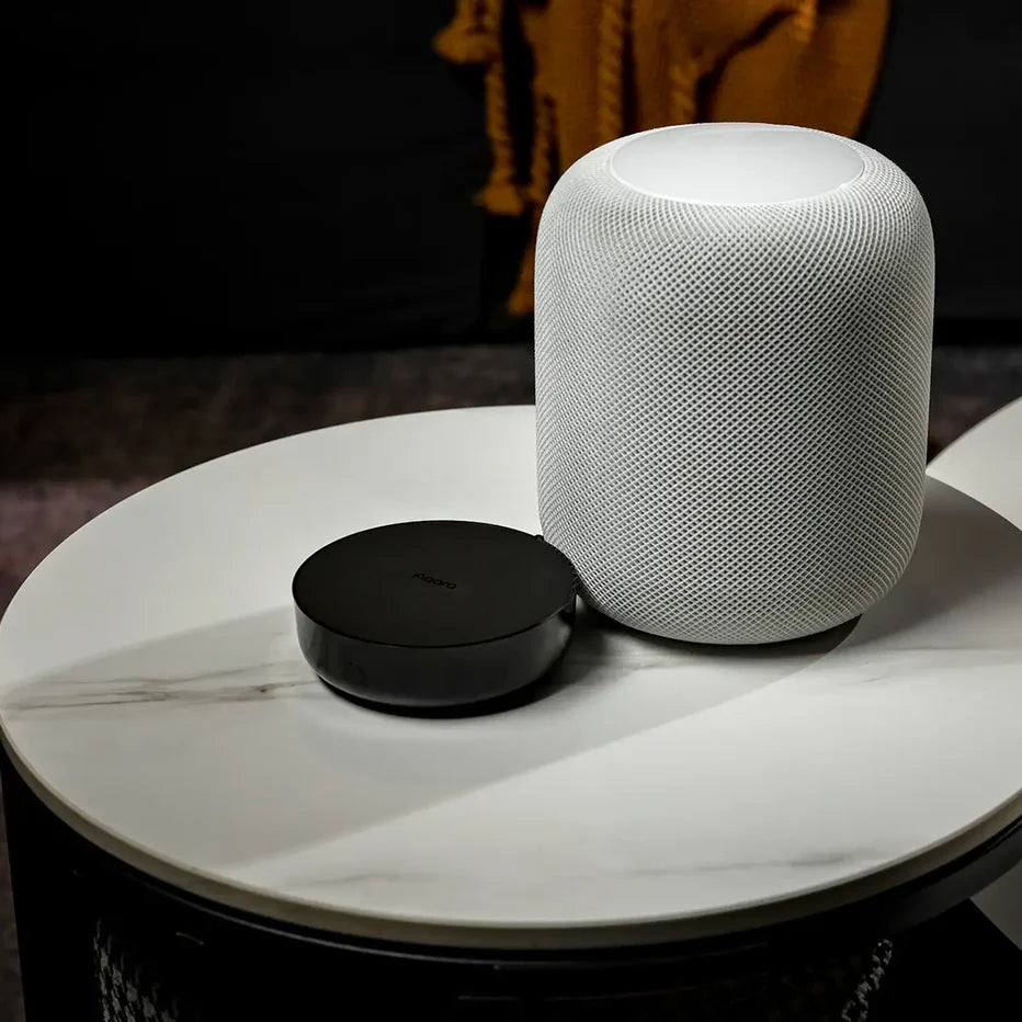 White smart speaker and black Aqara M2 Hub on a marble surface with a blurred background